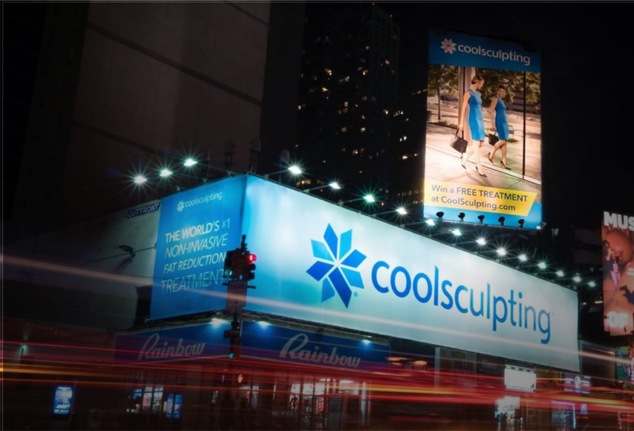 CoolSculpting billboards lit up at night over the Rainbow store corner in Times Square, New York