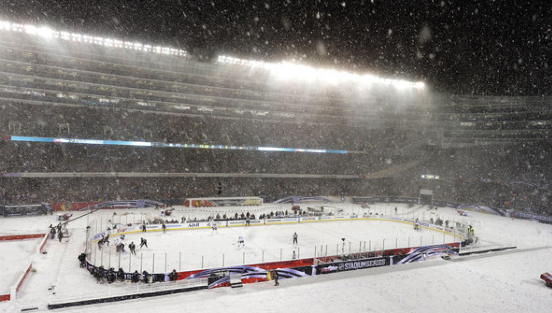 Snow falling over the outdoor rink at Soldier Field during the 2014 NHL Stadium Series, packed stadium under the lights
